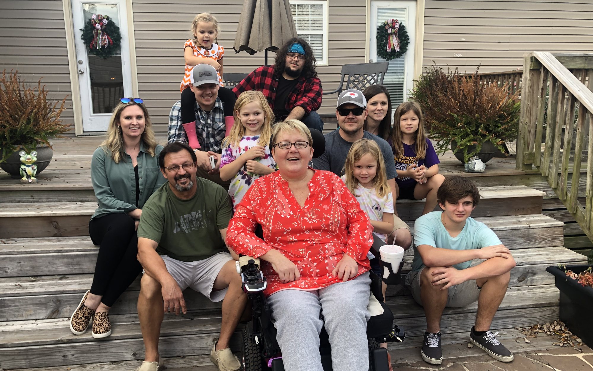 Charlotte Baker in her wheelchair, smiling, surrounded by her family on the back porch steps