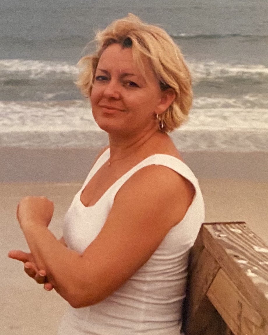Charlotte Baker smiling on the beach beside a wooden boardwalk railing