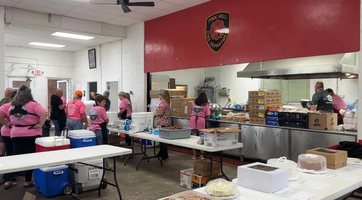 Volunteers in pink memorial shirts preparing barbecue plates at the Pink Hill Fire Department